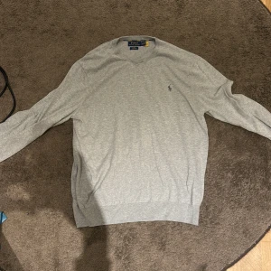 Grå slim fit tröja från Polo Ralph Lauren - Snygg grå långärmad tröja från Polo Ralph Lauren i slim fit-modell. Tillverkad i mjuk pima bomull och har den klassiska broderade loggan på bröstet. Perfekt för dig som gillar stilrena och enkla plagg med premiumkänsla.