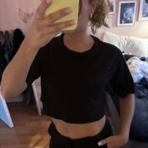 Svart croppad t-shirt från Monki - En svart croppad t-shirt från Monki i mjuk bomull. T-shirten har rund halsringning och korta ärmar, perfekt för en chill och enkel stil. Passar dig som gillar basic plagg med en modern twist.