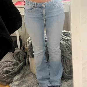 Ljusblå bootcut jeans - Säljer ett par ljusblå jeans med bootcut-modell och klassisk femficksdesign. Jeansen har låg midja och är tillverkade i mjukt denimtyg som sitter snyggt över höfterna och låren innan de släpper ut vid bensluten. Perfekta för en avslappnad och trendig look.