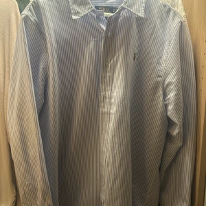 Randig skjorta från Polo Ralph Lauren - Snygg blåvit randig skjorta från Polo Ralph Lauren i klassisk passform. Skjortan har långa ärmar, knappar framtill och är tillverkad i bomull. Perfekt för dig som gillar en clean och tidlös stil.