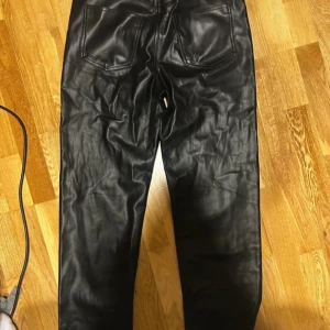 Svarta skinnbyxor Gina Tricot 38 - Snygga svarta skinnbyxor från Gina Tricot i storlek 38. Byxorna har raka ben, klassiska bakfickor och en stilren look. Perfekta för dig som vill ha en edgy vibe och gillar att sticka ut med material som ser ut som äkta skinn.