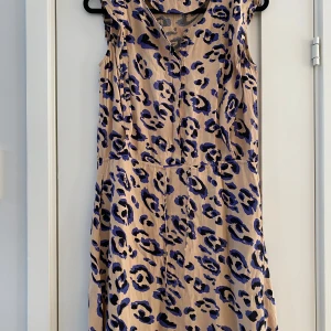 Leopardmönstrad klänning från InWear - Cool ärmlös klänning från InWear med beige botten och blåsvart leopardmönster. Klänningen har v-ringning och knappar framtill, samt en lätt utställd kjol. Perfekt för dig som vill sticka ut med ett djurmönster och en avslappnad men trendig look.