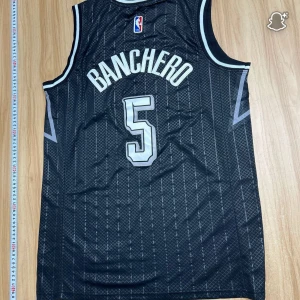 Orlando Magic Banchero #5 baskettröja - Snygg svart baskettröja från Nike med Orlando Magic-tryck och Banchero #5 på ryggen. Tröjan är ärmlös med vita och grå detaljer, diskret mönster och officiella NBA-loggor. Perfekt för dig som vill ha en cool och autentisk look på planen.
