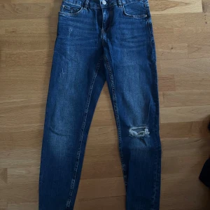 Blå super skinny jeans från Bershka - Säljer ett par blå super skinny jeans från Bershka i storlek 34. Jeansen har regular waist, klassisk femficksmodell och slitning med hål på ena knät. Tillverkade i stretchig denim.