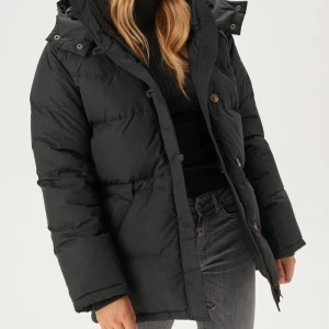 Svart dunjacka med huva och knappar - Köpt för 6000 STRL: XXXS, PASSAR SOM XS OCH S!                                Snygg svart boomerang dunjacka med huva och stora knappar framtill. Jackan har en quiltad design, dragkedja och praktiska fickor på sidorna. Perfekt för kalla dagar och har en klassisk, lite längre passform som håller dig varm hela vintern. 