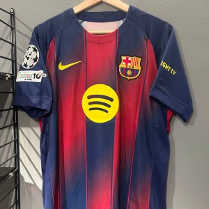FC Barcelona Cubarsí matchtröja - Snygg FC Barcelona matchtröja med Cubarsí och nummer 2 på ryggen. Tröjan har klassiska blå och röda ränder, gula detaljer och klubbmärke på bröstet. Spotify-logga i gult framtill och Champions League-patch på ärmen. Tillverkad i lätt och ventilerande polyester. Helt ny med tagg en replika