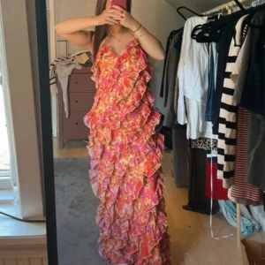 Blommig volangklänning i rosa och orange - Superfin långklänning med blommigt mönster i rosa, orange och rött. Står storlek xxs men rymlig så passar bättre xs 