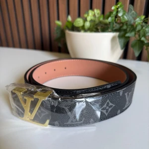 Louis Vuitton svart skärp med monogram (15) - Louis Vuitton bälte i svart skinn med klassiskt monogrammönster i grått och stor LV-spänne i guld. Insidan är beige och har snygga sömmar. Perfekt accessoar för att lyfta din outfit med lyxig vibe.