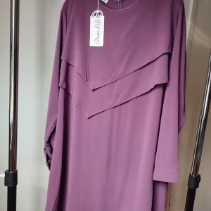 Plommonsfärgad långklänning från Dress Life I Nyskick - Säljer en plommonsfärgad långklänning från Dress Life med snygga lager på framsidan och långa ärmar. Klänningen har pärlknapp vid ärmslut. Materialet känns lätt och flowy, perfekt för dig som gillar stilrena och eleganta plagg. Strök 42 ( Turkisk strlk 44)