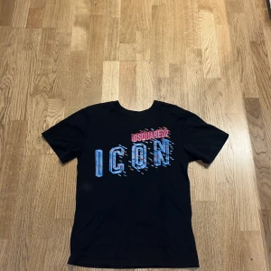 Svart Dsquared2 ICON t-shirt - Svart t-shirt från Dsquared2 med stor, färgglad 'ICON'-print i blått, rött och grönt på bröstet. Klassisk rund hals och korta ärmar. Materialet är mjuk bomull som känns skön mot huden. Perfekt för dig som gillar streetstyle och vill sticka ut med en cool logga. Köpt för 850 använd ganska mycket 