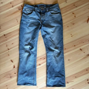 Vintage Nudie jeans modell bootcut ola - Säljer ett par ljusblå jeans från Nudie modell bootcut ola som är en äldre bootcut model från nudie som inte säljs längre. Jeansen har raka ben och normal passform och lite bootcut i slutet av jeansen, samt Nudies ikoniska broderi på bakfickorna. Perfekta för en avslappnad och cool stil.