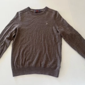 Brun stickad tröja från Morris - Säljer en klassisk grå stickad tröja från Morris i 100% merinoull. Tröjan har rund halsringning, ribbade muddar och en liten broderad logga på bröstet. Perfekt för lager-på-lager och enkel att matcha med det mesta. Står att de är M men passar nog bäst på en XS. Två noppor som syns på bilderna annars en fin tröja. 