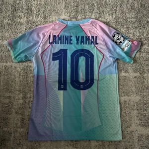 FC Barcelona Lamine Yamal Nike tröja - Säljer en FC Barcelona fotbollströja med Lamine Yamal och nummer 10 på ryggen. Tröjan är kortärmad och har ett unikt mönster i ljusblått, lila och rosa med klubbmärke, Nike-logga och Spotify som sponsor. Materialet är lätt och andas, perfekt för match eller träning. Kan diskutera om pris