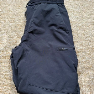 Svarta softshellbyxor - Endast använd fåtal gånger. Svarta byxor i mjukt och stretchigt material med elastisk midja och dragkedjeficka på benet. Snygg, enkel design med förstärkta knän och smal passform,Perfekta för uteliv eller chill dagar. Liknande treckmates byxor pm för frågor