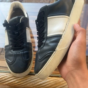 Valentino Garavani Mörk Blåa sneakers - Snygga sneakers från Valentino Garavani i svart och vitt skinn. Klassisk låg modell med rund tå, svarta snören och vit platt sula. Perfekt för dig som gillar stilrena och exklusiva sneakers med lyxig känsla. Diskret logga på plösen och cool kontrast mellan färgerna. Dessa är original men förra sulan gick av så dem byttes
