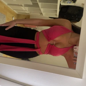 Rosa omlott halterneck topp - Säljer en rosa omlott halterneck topp med ringdetalj framtill. Toppen är croppad och har långa band som knyts runt midjan. Materialet känns mjukt och stretchigt. 