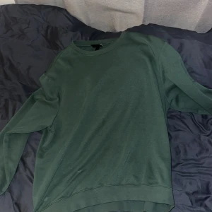 Mörkgrön sweatshirt i bomull - Enkel och stilren mörkgrön sweatshirt med rund halsringning och långa ärmar. Tröjan är tillverkad i mjuk bomull och har en relaxed passform som passar perfekt till jeans eller mjukisbyxor.