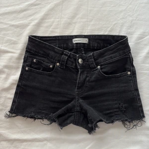Svarta jeansshorts  - Svarta jeansshorts med råa, fransiga kanter och klassisk femficksdesign. Shortsen har knapp och dragkedja framtill samt snygga fickor med lock och knapp bak. Perfekt för dig som gillar en edgy och avslappnad stil.