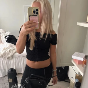 Svart offshoulder topp från JDY - Säljer en svart offshoulder topp från JDY i storlek S. Toppen är croppad med smockad, ribbad struktur och har korta ärmar. Den har volangdetaljer vid halsringning och ärmslut som ger en söt vibe. Perfekt att styla med jeans eller kjol för en trendig look.