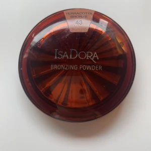 IsaDora Bronzing Powder Terracotta Bronze - IsaDora Bronzing Powder i nyansen 43 Terracotta Bronze. Kommer i en rund, brun plastförpackning med spegel och mjuk vit applikator med svart IsaDora-band. Ger en varm, solkysst glow med bronzig finish. Fragrance free och kliniskt testad. Innehåller 10 g.