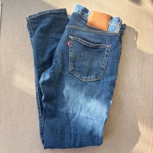 Levi's 511 blå jeans  - Säljer ett par klassiska Levi's 511 jeans i blå denim. Modellen är slim fit med raka ben och normal midja. Jeansen har fem fickor, Levi's ikoniska läderpatch bak och röda logotag på bakfickan. Perfekta för en clean och tidlös look.