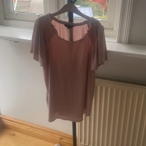 Ljusrosa blus från Banana Republic - Supersöt ljusrosa blus från Banana Republic med rynkade detaljer vid axlarna och volangkant runt halsen. Blusen har korta, luftiga ärmar och är tillverkad i ett mjukt, lätt material som ger en flowy känsla.