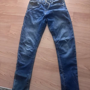 Blå jeans från LAB Industries - Säljer ett par blå jeans från LAB Industries i storlek 170. Jeansen har klassisk femficksdesign, dragsko i midjan och är tillverkade i en stretchig mix av bomull, polyester och elastan. Snyggt slitna detaljer och smal passform för en modern look.