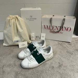 Valentino Garavani Open sneakers vit/grön - Säljer ett par Valentino Garavani Open sneakers i vitt skinn med en bred grön rem över mitten. Klassisk rund tå, vita snören och ikoniska nitar baktill på sulan. Kommer med dustbag, originalpåse, valentino garavani brev och två olika kort. Sparsamt använda i ungefär en månad men nu börjar de bli för små. Riktigt snygga trendiga och sneakers perfekta för vintern!
