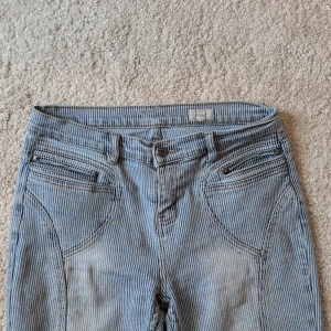 Randiga bootcut jeans från Jeans - Nu är mina Snygga ljusblå och vita randiga bootcut jeans från Jeans. Byxorna har klassisk femficksdesign, låg midja och är tillverkade i ett mjukt bomullsmaterial. Perfekta för dig som gillar retrovibbar och vill sticka ut med ett unikt mönster. Midjemått: 37cm Innerbenslängd: 78cm