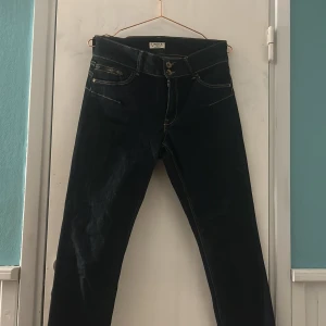 Mörkblå jeansbyxor från Lindex - Snygga mörkblå jeansbyxor från Lindex med klassisk femficksdesign och kontrastsömmar. Byxorna har normal passform och raka ben, stängs med dragkedja och dubbla knappar. Perfekta för dig som gillar stilrena och enkla jeans.