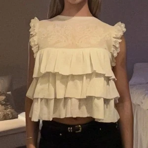 Vit blus med volanger och spets - Säljer en söt vit blus med flera lager volanger framtill och baktill.