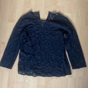 Svart spetsblus från Mango Suit - Säljer en svart blus från Mango Suit i storlek M. Blusen är helgjord i transparent spets med blommigt mönster och lätt loose passform. Spännet är löst men går att fixa med sykunskaper.