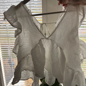 Vit volangblus med knyt i ryggen - Supersöt vit blus med volanger och v-ringning. Blusen har knyt i ryggen och fina spetsdetaljer längs kanterna. Använd endast en gång! Från Zara! Hör av er vid eventuella frågor 🩷