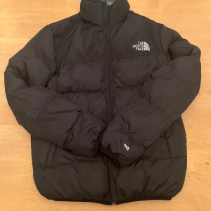 The North face puffer - The North Face Pufferjacka – Svart Stilren och varm pufferjacka från The North Face. Den är perfekt för kyliga dagar och håller dig både bekväm och snygg. Jackan är i bra skick, med endast ett litet hål längst ner i dragkedjan. Hålet påverkar inte funktionaliteten, och jackan är fullt användbar. Storlek: small Färg: Svart Detaljer: snygg Heltäckande dragkedja Kompakt och lättviktig Klassisk design med det välkända The North Face-loggan Skick: Mycket bra, förutom ett litet hål vid dragke