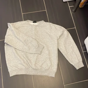 Grå sweatshirt från H&M - En enkel och stilren grå sweatshirt från H&M i storlek L. Tröjan har rund hals, ribbade muddar vid ärmslut och nederkant samt långärmad passform. Perfekt för chill dagar och passar till allt. Materialet är mjuk bomullsmix.