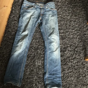 Blå jeans från Nudie Jeans Co - Snygga blå jeans från Nudie Jeans Co med klassisk femficksdesign och orangea sömmar. Jeansen har en rak passform och är tillverkade i slitstarkt denim. Det var ett hål på framsidan som jag har sytt,jeansen passar dig som är runt 160
