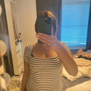 Randig ribbad topp med öppen rygg - Säljer en vit och svart ribbad topp med smala ränder och fyrkantig ringning. Toppen har korta ärmar och en snygg öppen rygg med detalj. Perfekt för dig som gillar trendiga och bekväma plagg med det lilla extra.