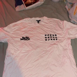 Vit loose fit t-shirt med stjärnor H&M - Säljer en vit t-shirt från H&M i loose fit med coola svarta stjärnor tryckta både fram och bak. På framsidan finns även texten 'S/S 202X'. T-shirten har korta ärmar och är gjord i mjuk bomull, perfekt för dig som gillar streetwear och oversized stil.