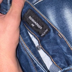 Blå Dsquared2 jeans herr, storlek 29/32 - Säljer ett par snygga blå jeans från Dsquared2 i herrmodell, storlek 29/32. Jeansen har slitna detaljer, klassisk femficksdesign och kontrastsömmar. Tillverkade i Italien med en cool tvätt och raka ben. Perfekta för dig som gillar streetwear och premiumkänsla.