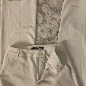 Beiga kostymbyxor från Bik Bok - Stilrena beiga kostymbyxor från Bik Bok med raka ben och klassisk passform. Byxorna har hällor för bälte, diskreta sidofickor och stängs med dragkedja och knapp. Perfekta för en clean och snygg look.