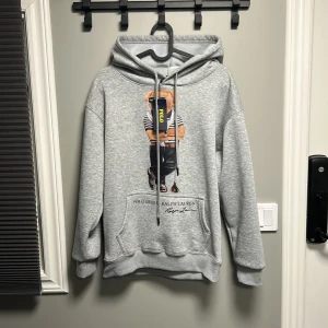 Grå polo bear hoodie  - Snygg grå hoodie från Polo Ralph Lauren med ikoniskt björntryck framtill. Insidan av tröjan har ett jätte skönt pälsliknande material, vilket gör tröjan perfekt att ha till hösten. Tröjan är helt ny med prislappen kvar. Jag säljer den då den tyävrr är för lite för mig. Kom privat om ni har fler frågor. Priset kan gå att diskutera. 
