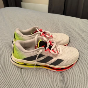 Adidas Adistar vita sneakers - Säljer ett par Adidas Adistar sneakers i vitt med svarta och neongula detaljer samt inslag av rött. Skorna har snörning, ventilerande mesh-ovandel och platt sula med extra dämpning. Perfekta för dig som gillar sportig stil och komfort.