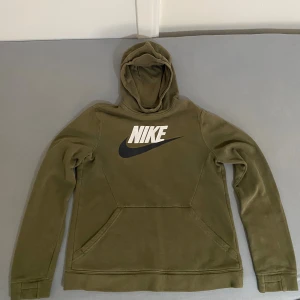 Nike hoodie herr XL – olivgrön – mycket bra skick - Säljer en original Nike hoodie i olivgrön färg, storlek XL (158–170 cm enligt etikett). Tillverkad i Kambodja. Hoodien är i mycket bra skick, utan fläckar, hål eller synligt slitage. Mjuk insida, klassisk Nike-logo på bröstet. Perfekt för vardag, gym eller streetwear.