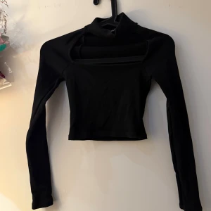 Svart croppad polotopp från Zara - Svart långärmad polotopp från Zara i croppad modell med cool cut-out detalj vid halsen. Toppens material är mjukt och stretchigt, perfekt för att skapa en edgy look. Snygg att styla med höga jeans eller kjol för en trendig vibe.