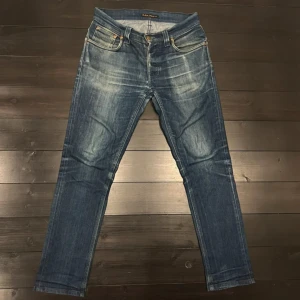 Nudie Jeans Grim Tim blå jeans 31/34 - Säljer ett par Nudie Jeans Grim Tim i blå tvätt med snygga slitningar. Byxorna är lagade i skrevet men inget som syns i bruk.