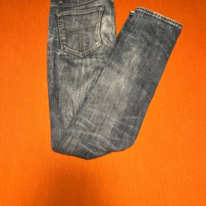 Tiger of sweden jeans - Säljer ett par blå jeans med snygga slitningar och hål på knäna. Jeansen har klassisk femficksdesign, raka ben och ljus tvätt med coola detaljer. Perfekt för dig som gillar en avslappnad och trendig stil.