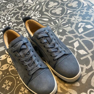 Blåa sneakers från Louboutin - Snygga blåa sneakers från Christian Louboutin i mocka med klassisk röd sula och vita detaljer. Skorna har rund tå, snörning och ventilerande metalldetaljer på sidan. Insidan är ljusbeige och sulan har Louboutins ikoniska logga. PRIS KAN DISKUTERAS VID SNABB AFFÄR  
