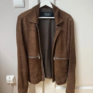 Brun mockajacka från Replay - Snygg brun mockajacka från Replay med klassisk krage och två stora fickor framtill med silvriga dragkedjor. Fick denna i present och den blev tyvärr för kort för mig efter aldeles för få användningar. Nypris och även slutsåld för 4000 kr på MQ!