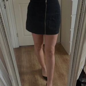 Svart kortkjol med dragkedja från H&M - Svart kortkjol från H&M Divided i storlek 36. Kjolen har en rak passform och är tillverkad i 100% bomull. Framtill finns en snygg silverfärgad dragkedja som detalj. 