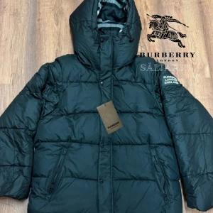 Burberry Puffer - Svart dunjacka från Burberry med klassisk Säljer en elegant och mångsidig Burberry-jacka i svart, i nyskick. Dunfodrad för värme och komfort med det klassiska rutmönstret i huvan som ger en exklusiv touch. Praktiska dragkedjefickor, avtagbar huva och diskret logopatch på ärmen. Passar M/L. Jackan är i princip som ny och utan defekter. En lyxig kombination av stil och funktion – perfekt för både vardag och tillfällen då du vill klä upp dig.  📦Snabb leverans - skickas samma dag📌